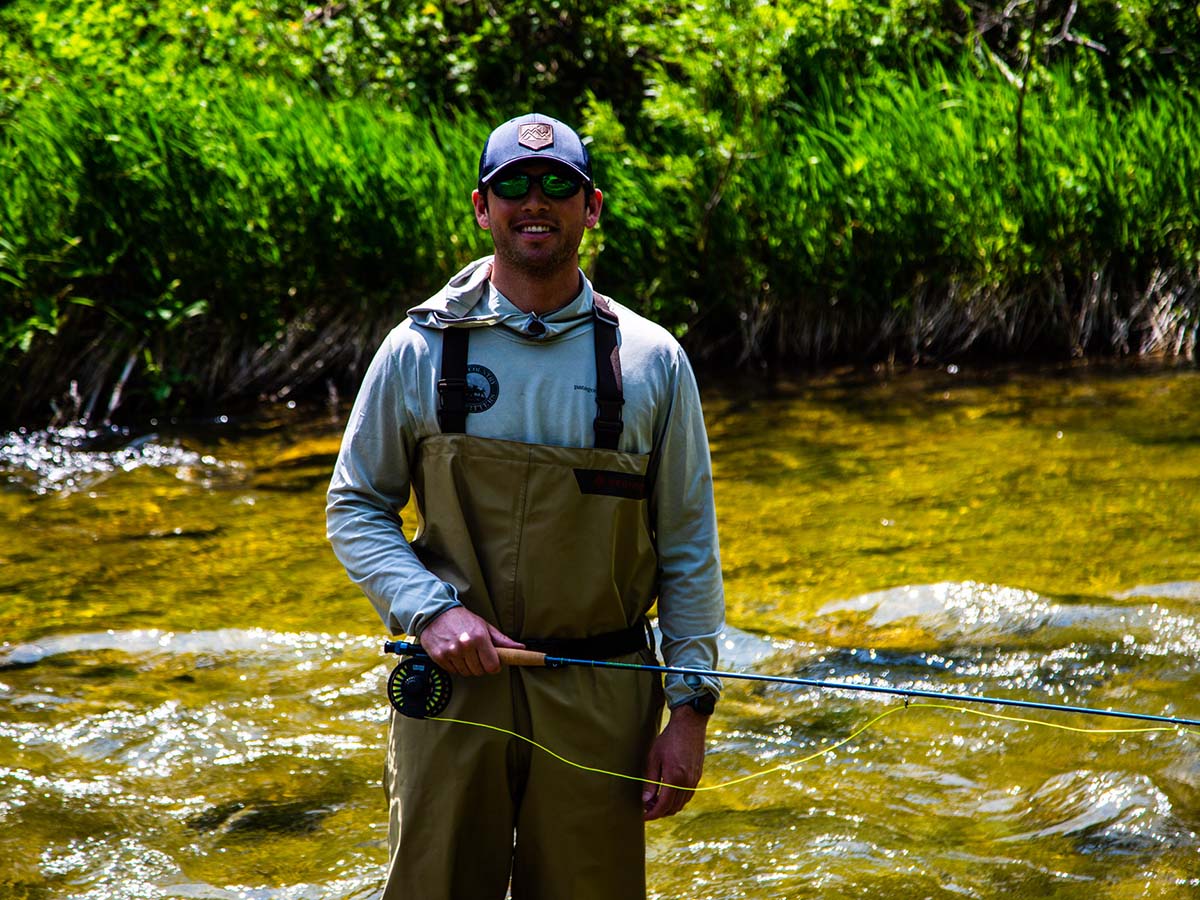 A man standing in a river smiling while fly fishing.