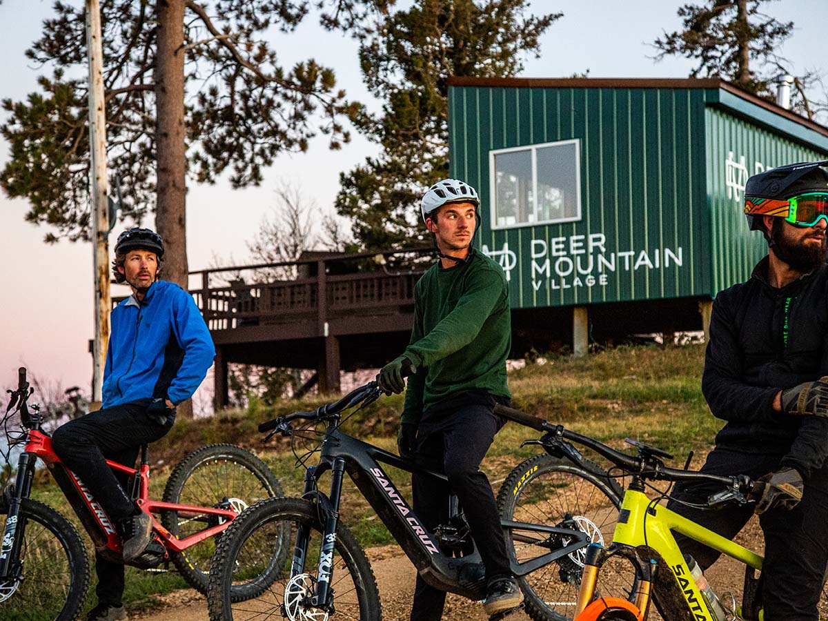 Three men mountain biking with a Deer Mountain Village trailer behind.